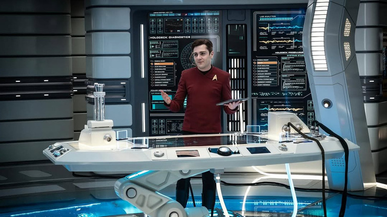 Martin Quinn as Scotty stands shrugging in front of a complicated instrument panel in Star Trek: Strange New Worlds