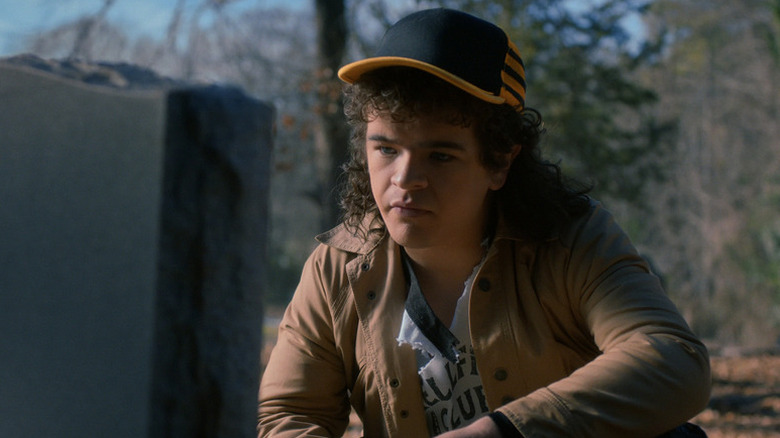 Dustin Henderson (Gaten Matarazzo) kneels in front of a tombstone in Stranger Things