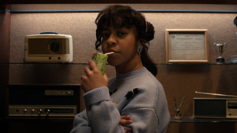 Erica drinking a juice box in front of a control panel in Stranger Things