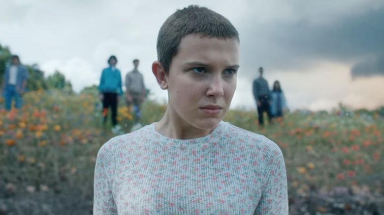 Eleven (Millie Bobby Brown) stood on a hill with other Stranger Things cast out of focus behind her