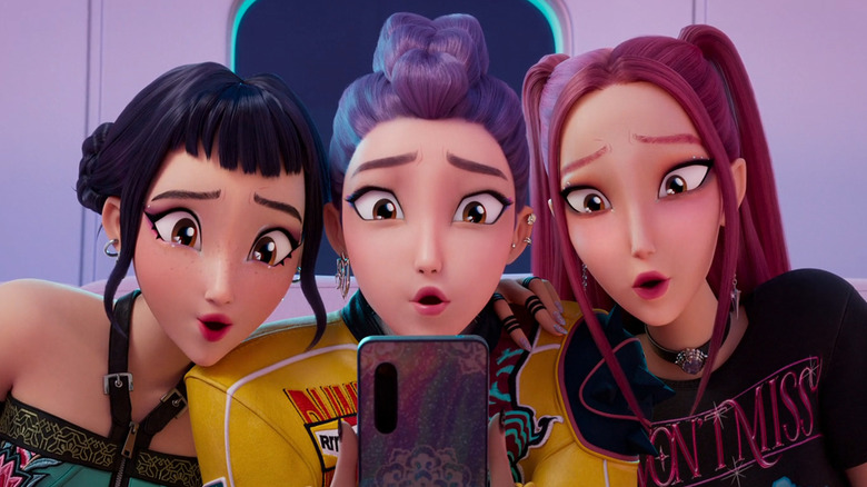 Zoey, Rumi, and Mira stare into a phone in KPop Demon Hunters