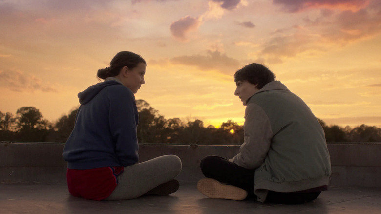 Millie Bobby Brown as Eleven and Finn Wolfhard as Mike sitting together in Stranger Things season 5