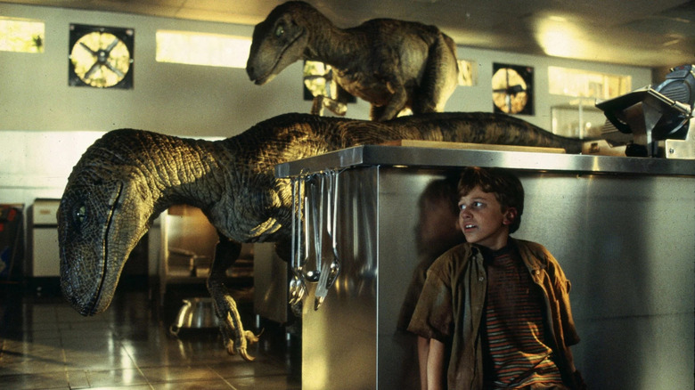Tim hides behind a kitchen counter while Velociraptors sniff around in Jurassic Park