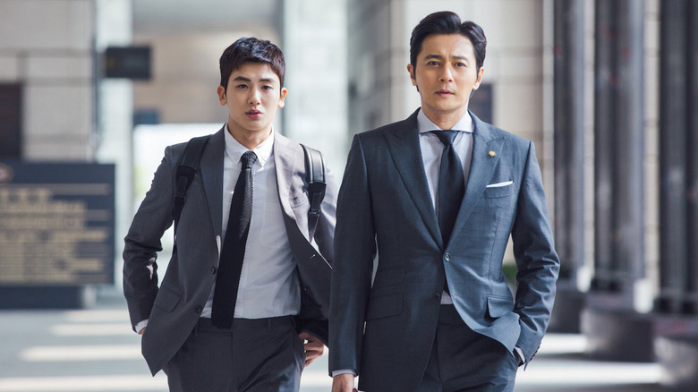 Go Yeon-woo (Park Hyung-sik) walks behind Choi Kang-seok (Jang Dong-gun) in a lobby in Suits