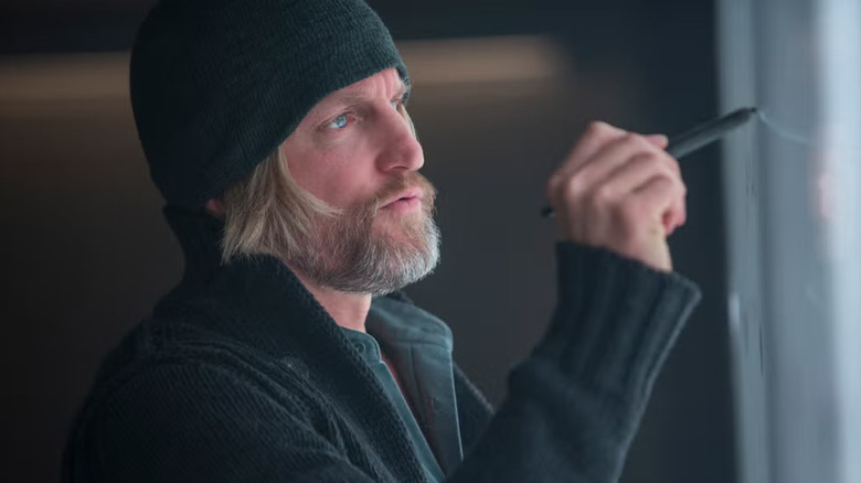 Haymitch in a black cap writing on a whiteboard in The Hunger Games: Mockingjay - Part 1