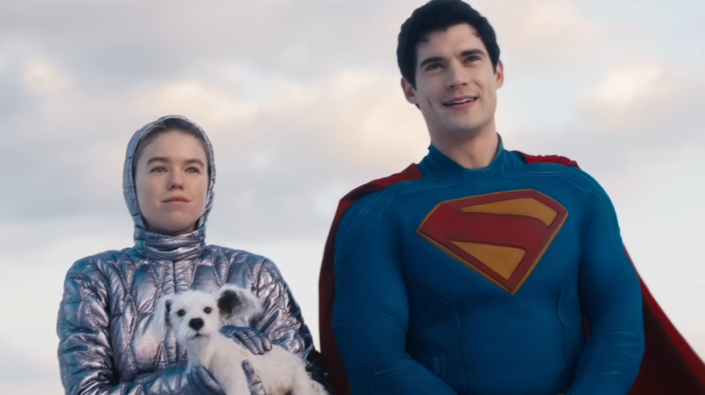 Milly Alcock as Supergirl wearing a futuristic parka and holding her dog Krypto next to David Corenswet as Superman in Supergirl