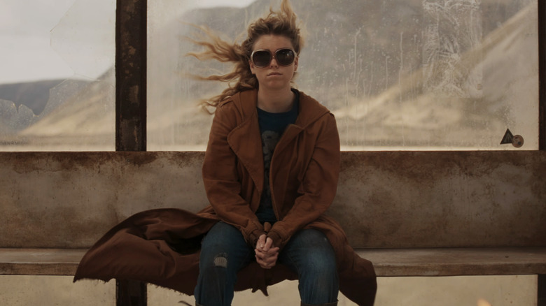 Milly Alcock as Kara sitting on a bench wearing sunglasses in Supergirl (2026)