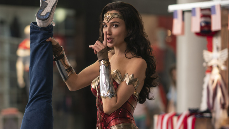 Gal Gadot dans le rôle de Wonder Woman avec son doigt jusqu'à la bouche tenant quelqu'un à l'envers dans Wonder Woman 1984