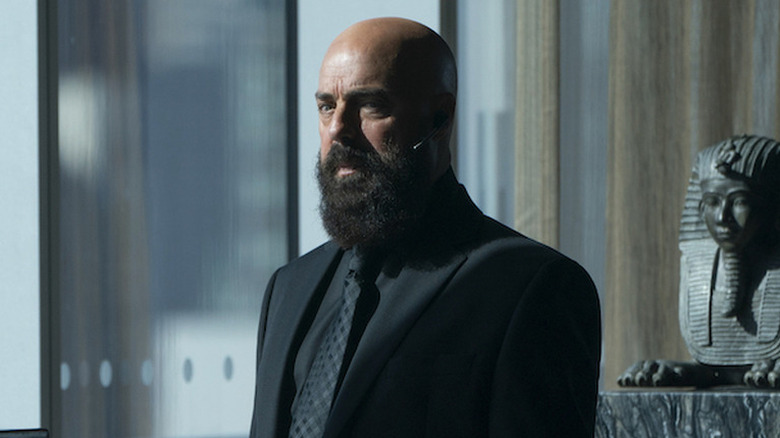 Titus Welliver as Lex Luthor, standing near statues on Titans