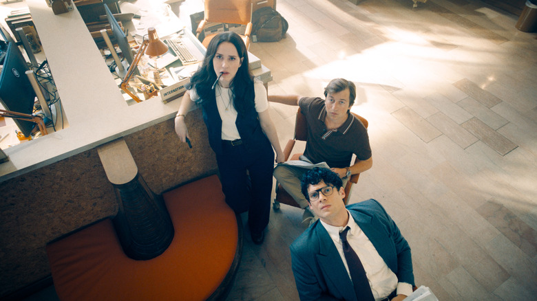Rachel Brosnahan as Lois Lane standing by a desk as Skyler Gisondo as Jimmy Olsen and David Corenswet as Clark Kent sit nearby in Superman