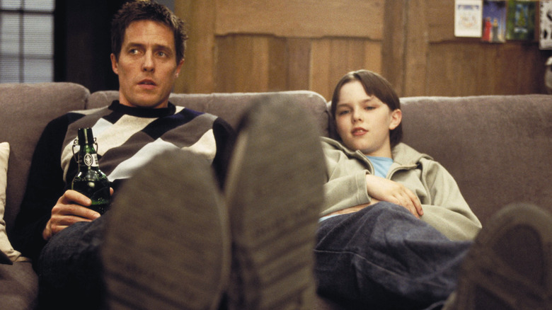 Will Freeman (Hugh Grant) sits on the sofa with (Marcus Brewer) Nicolas Hult in about one boy