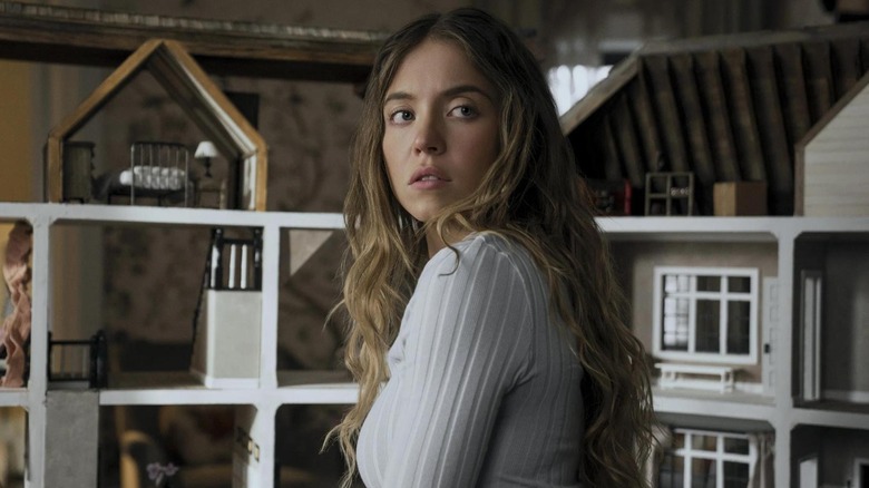 Sydney Sweeney as Millie looking over her shoulder in front of a dollhouse in The Housemaid