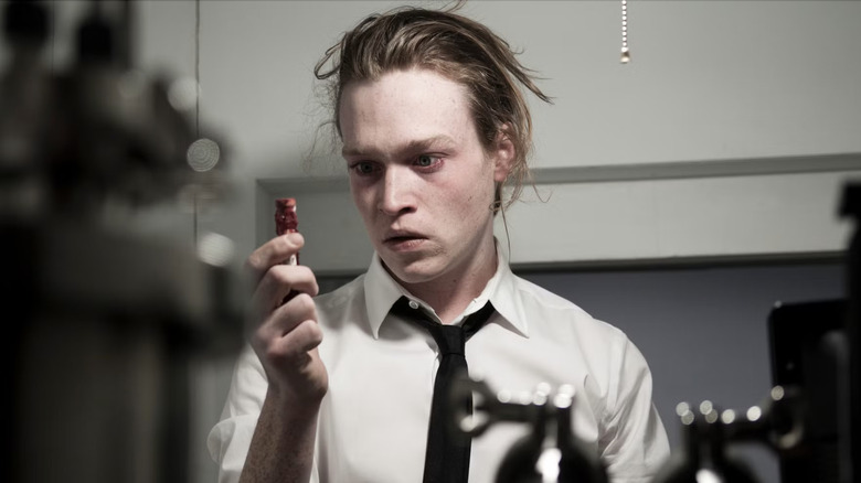 A frazzled-looking Syd March stares at a small red object he's holding in his hand in Antiviral