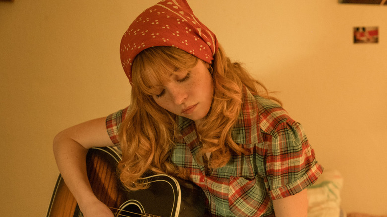 Sydney Sweeney as Penny Jo playing guitar on her bed in Americana