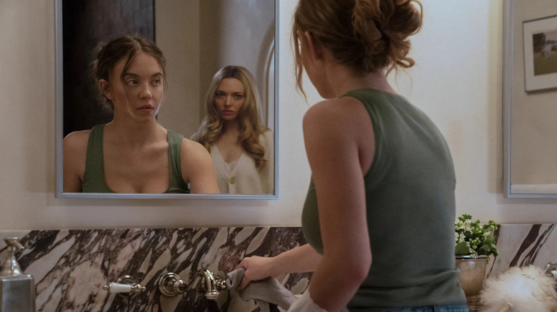 Millie cleaning with Nina behind her in the mirror in The Housemaid