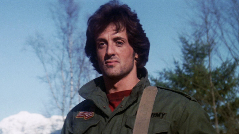 Sylvester Stallone's John Rambo stands looking into the distance against a blue sky in First Blood