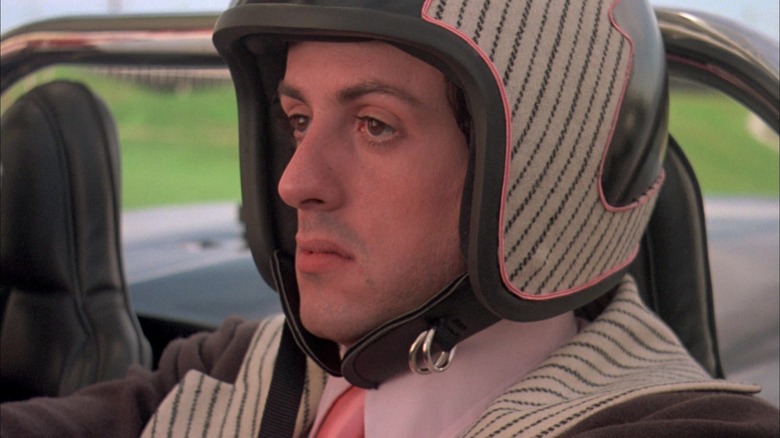 Sylvester Stallone as Joe 'Machine Gun' Viterbo sits in his car wearing a helmet in Death Race 2000