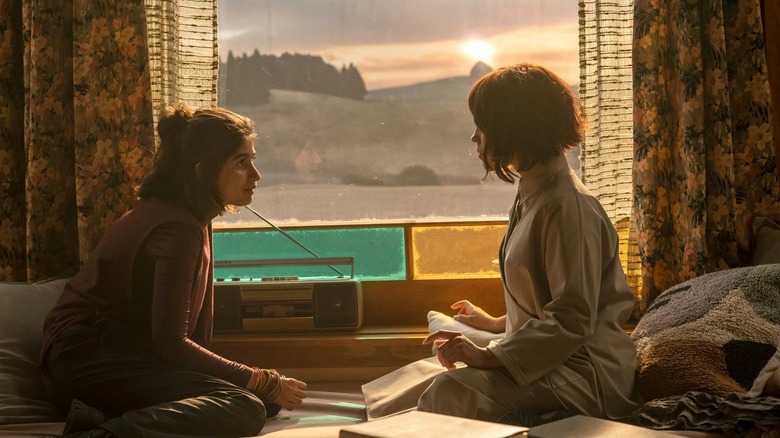 Mia Tharia as Josie sitting on the bed facing Jenna Ortega as Klara in Klara and the Sun