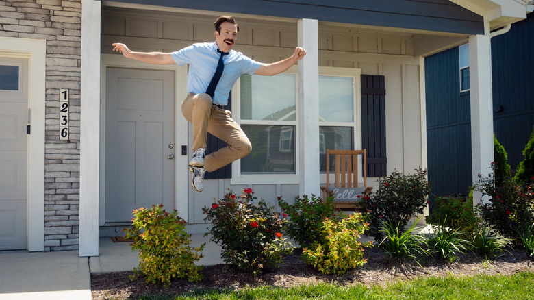 Ted Lasso joyously leaping over some bushes in front of a suburban house in Ted Lasso Season 4