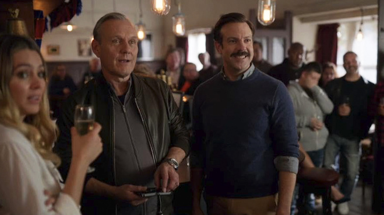 Rupert, Ted, and Bex stand next to each other in Mae's pub in Ted Lasso