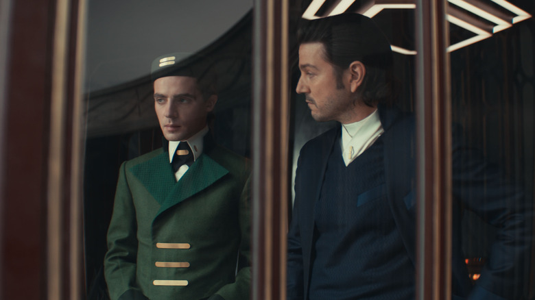 Diego Luna as Cassian Andor and Stefan Crepon as the bellhop Thela standing by a window in Andor