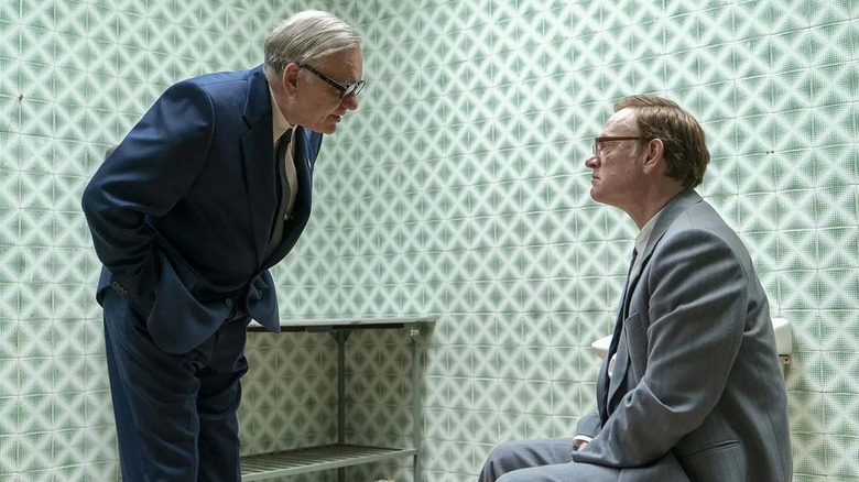 Jared Harris as Valery Legasov sitting down in front of a man who is bending over to speak to him in Chernobyl