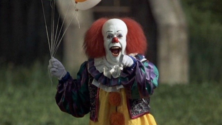 Tim Curry as Pennywise holding balloons and pointing with his mouth open in It (1990)