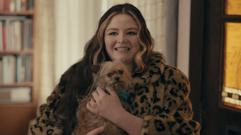 Megan Stalter as Cora holding a dog while wearing a fau-fur coat in Cora Bora