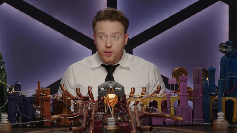 Brennan Lee Mulligan wearing a tie and sitting behind an elaborate map in Dimension 20