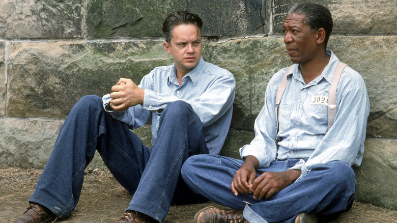 Andy Dufresne and Red sit against the wall of Shawshank Penitentiary talking in their prison uniforms in The Shawshank Redemption