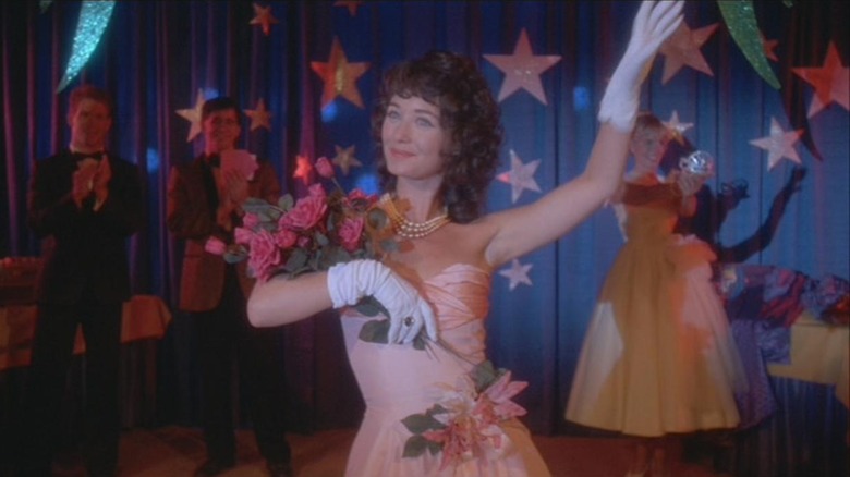 Lisa Schrage as Mary Lou Maloney in Hello Mary Lou: Prom Night II, on stage with a bouquet and waving.