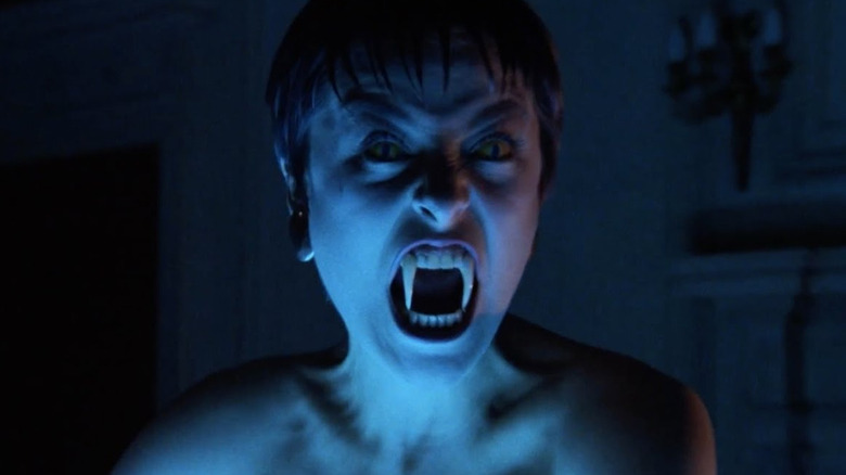 Amanda Donohoe as Lady Sylvia Marsh, in her human-serpent form wielding her fangs in front of a fiery background in The Lair of the White Worm, standing in some kind of wicker container.
