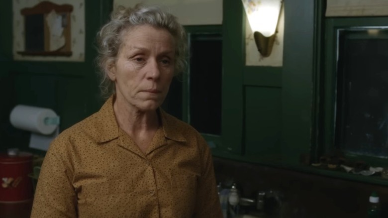 Frances McDormand as Olive Kitteridge standing with a gloomy expression on Olive Kitteridge