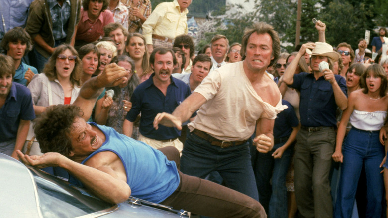 Philo Beddoe (Clint Eastwood) punches Jack Wilson (William Smith) against a car hood before a cheering crowd in Any Which Way You Can