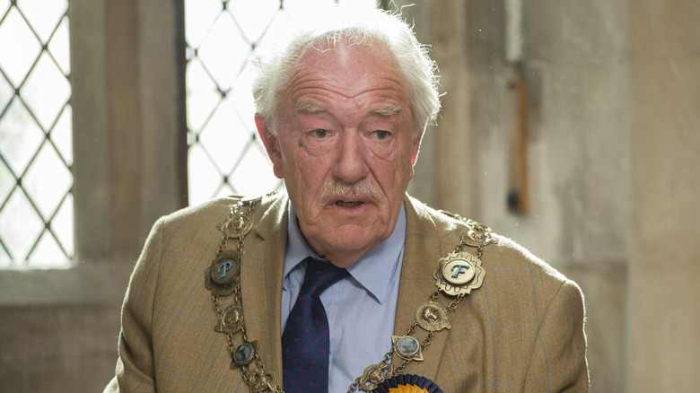 Michael Gambon as Howard Mollison in a suit and tie talking on The Casual Vacancy
