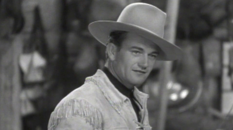 John Wayne donning a cowboy hat and jacket as John Trent in The Telegraph Trail, looking off frame.