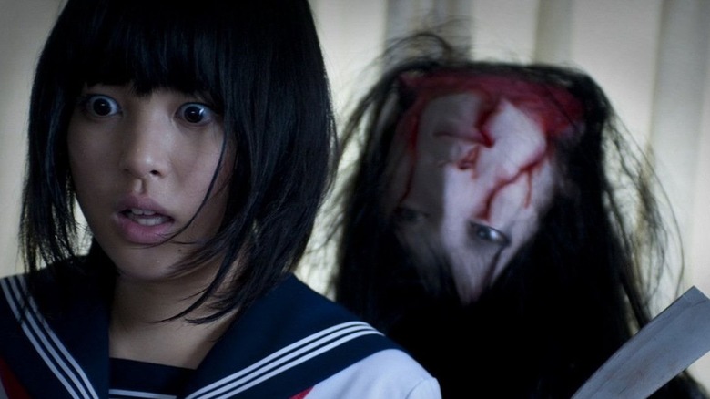 A girl looks offscreen as an upside down head approaches her with a knife