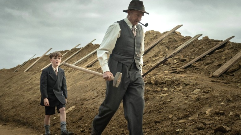 Ralph Fiennes as Basil Brown and Archie Barnes as Roberty Pretty walk in the dig site in The Dig