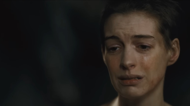 Anne Hathaway as Fantine with short hair, dirty face with tears streaming down it looking despondent in Les Misérables