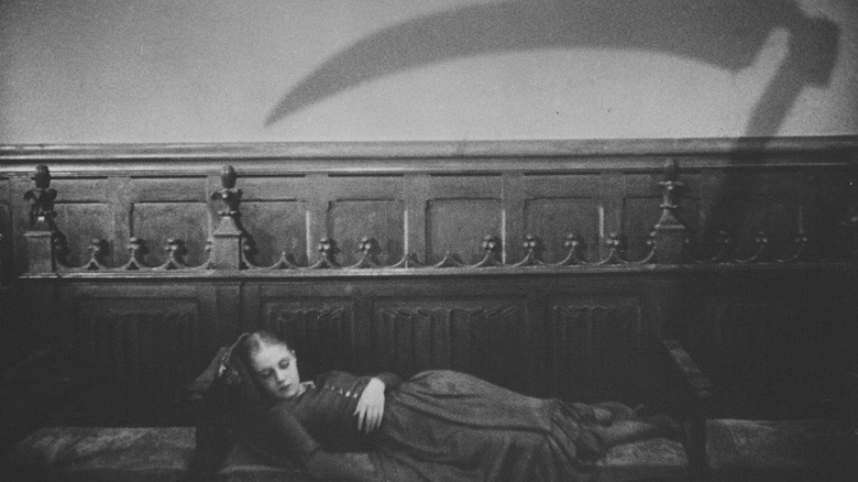 A woman lies under the shadow of a scythe