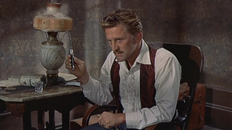 Doc Holliday (Kirk Douglas) sits in a chair holding a knife in Gunfight at the O.K. Corral