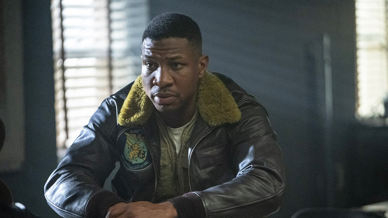 Jesse L. Brown (Jonathan Majors) sits in a darkened office wearing his bomber jacket in Devotion (2022)