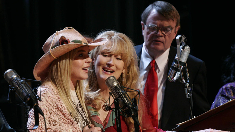 Lindsay Lohan as Lola singing in to microphone next to Meryl Streep as Yolanda and Garrison Keillor in Prairie Home Companion