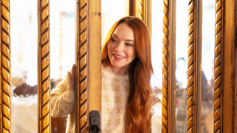 Lindsay Lohan as Sierra smiling as she enters a large wood and glass doorway in Falling for Christmas