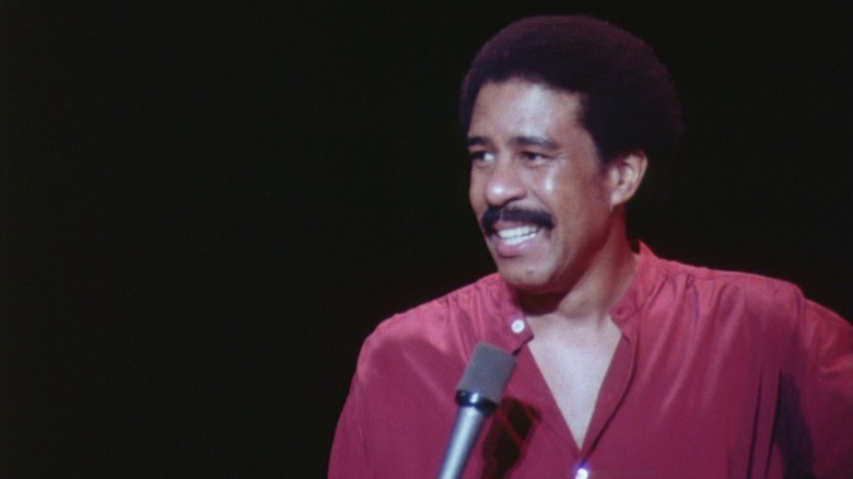 Richard Pryor grins holding a mic on stage in Richard Pryor: Live in Concert