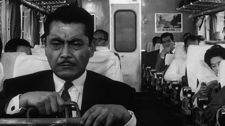Toshiro Mifune as Kingo Godo sitting in a train and holding a suitcase with an anguished expression on his face in High and Low