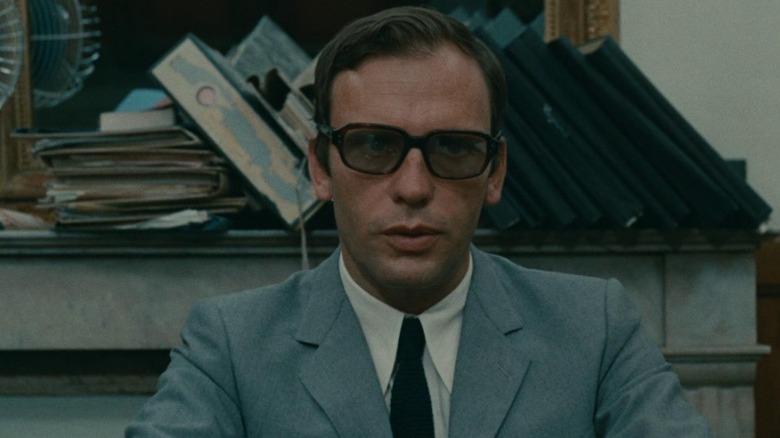 Jean-Louis Trintignant as the Examining Magistrate sitting in front of a jumble of folders on a shelf in Z