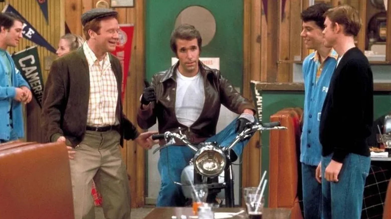 Fonzie (Henry Winkler) rides into a diner on a motorcycle as his friends watch on Happy Days