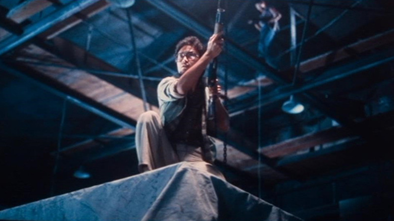 A man crouches on a structure in a warehouse with a gun in his hand in Men from the Gutter