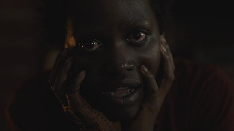 Lupita Nyong'o as Red from Us, mostly in shadow, her head in her hands, eyes wide